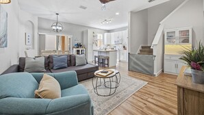 A modern living room with a sofa, a coffee table, and a dining area with a kitchen in the background. - Regal Palms 4BR Home: Water Park Fun! (Davenport)