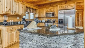 Cocina con armarios de madera, encimeras de granito, una isla de piedra, electrodomésticos de acero inoxidable y un salpicadero de piedra.