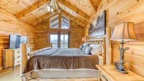 Un dormitorio de cabaña de madera con cama, televisión, lámpara y ventana.