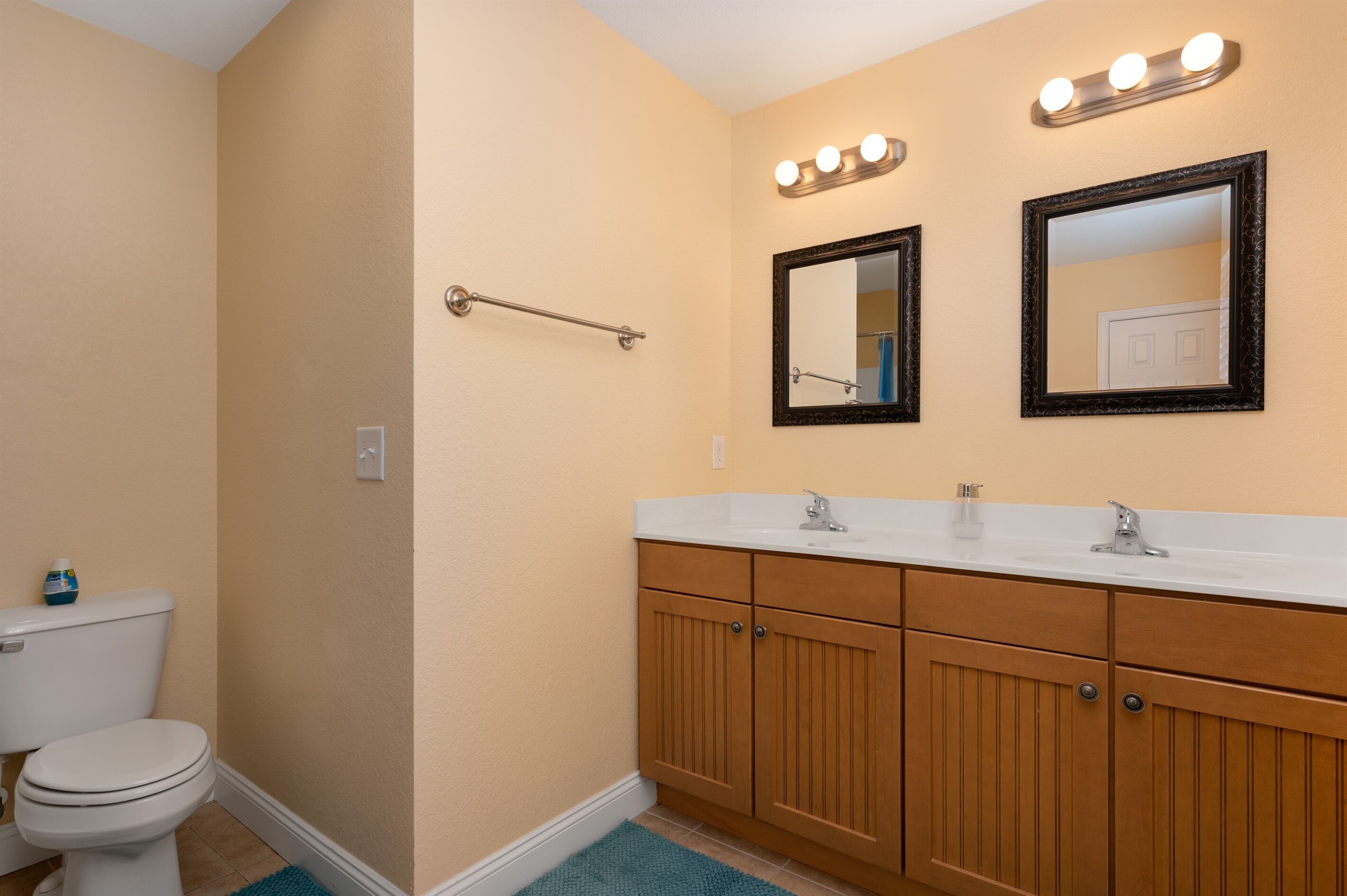 A bathroom with a toilet, wooden cabinets, a sink, and two mirrors.