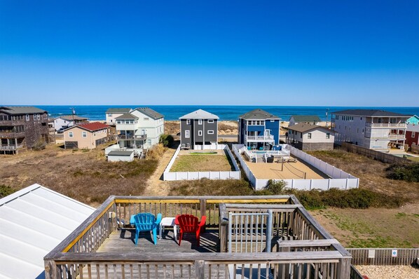 A coastal residential area with houses, a deck with chairs, and a view of the ocean.