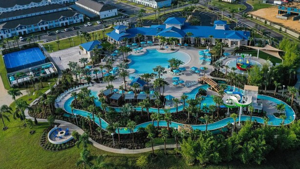 An aerial view of a resort with a large central pool, multiple smaller pools, and a water park area.