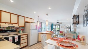 A modern kitchen with wooden cabinets, a central island, and a dining area with a table set for two. - Retro-Themed Condo | 2BR | Perfect Location (Myrtle Beach)