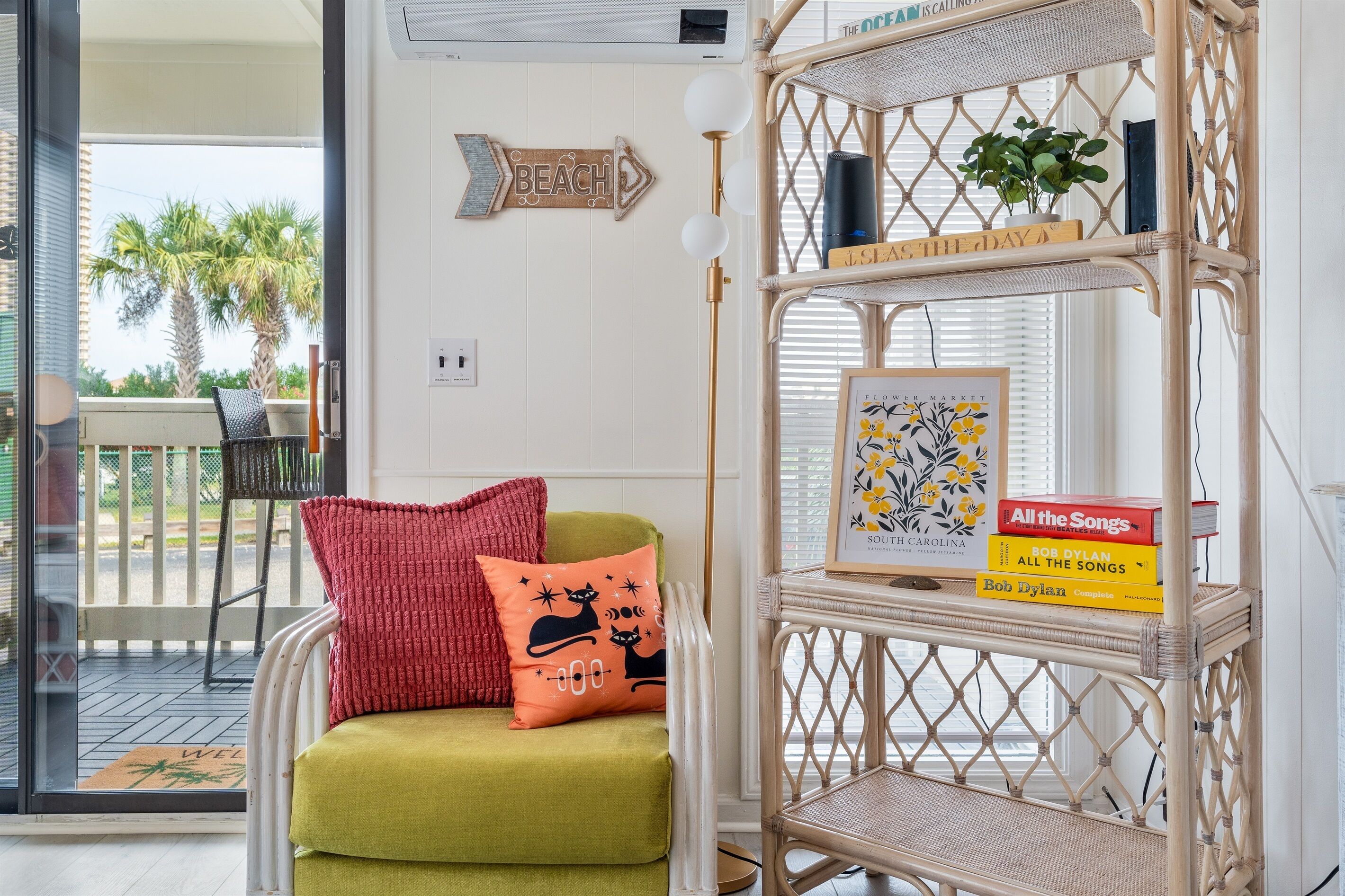 A room with a wicker chair, a red and yellow cushion, a bookshelf with books, and a 'Beach' sign on the wall.