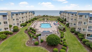 A hotel with a central pool surrounded by lounge chairs and umbrellas, multiple balconies, and a view of the beach. - Retro-Themed Condo | 2BR | Perfect Location (Myrtle Beach)