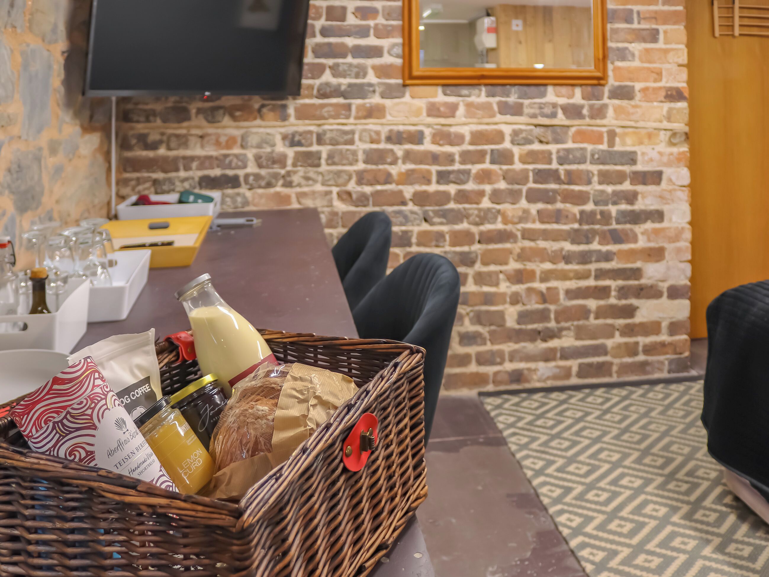A dining area with a brick wall, a television mounted above a table, and a wicker basket containing food and drinks.