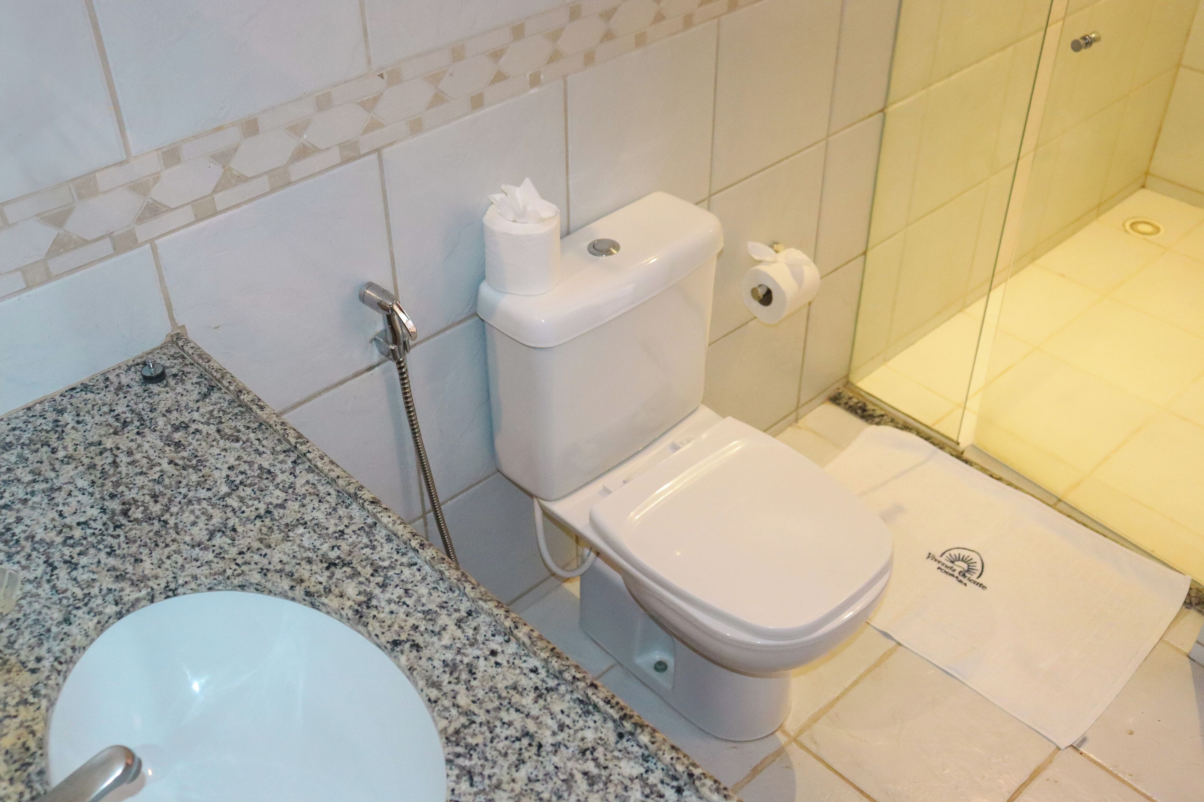 Casa de banho com sanita branca, lavatório e zona de duche.