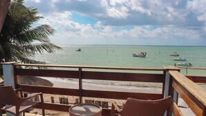 Vista al mar desde un balcón con sillas de mimbre, una mesita y un cubo de basura.