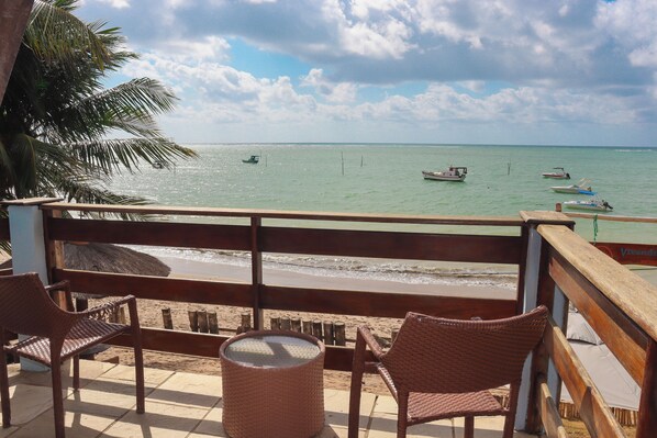 A beach view from a balcony with wicker chairs, a small table, and a trash bin. - Pousada Vivenda Oriente (São José da Coroa Grande)
