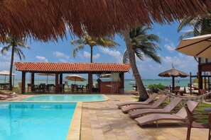 A pool area with lounge chairs, a bar, and a view of the ocean. - Pousada Vivenda Oriente (São José da Coroa Grande)