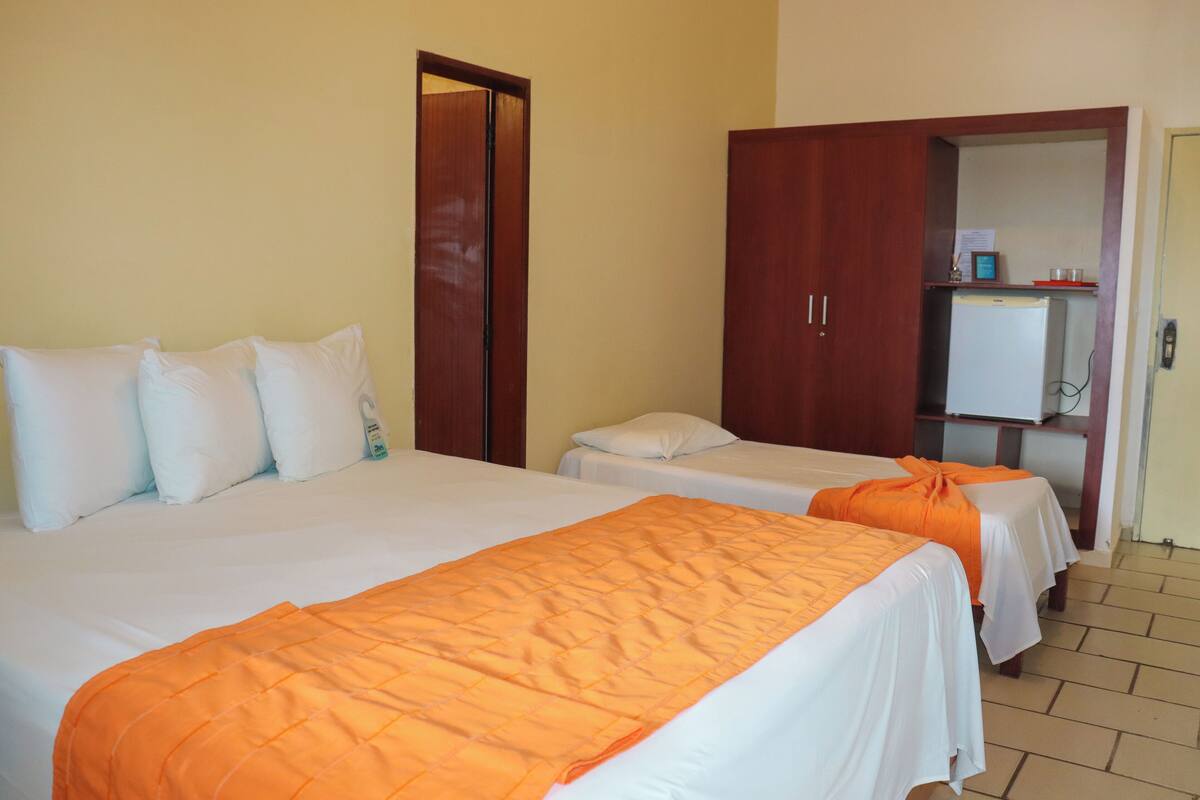 Een hotelkamer met twee bedden, elk voorzien van witte lakens en oranje dekens. Er staat een houten garderobe en een kleine koelkast in de hoek.