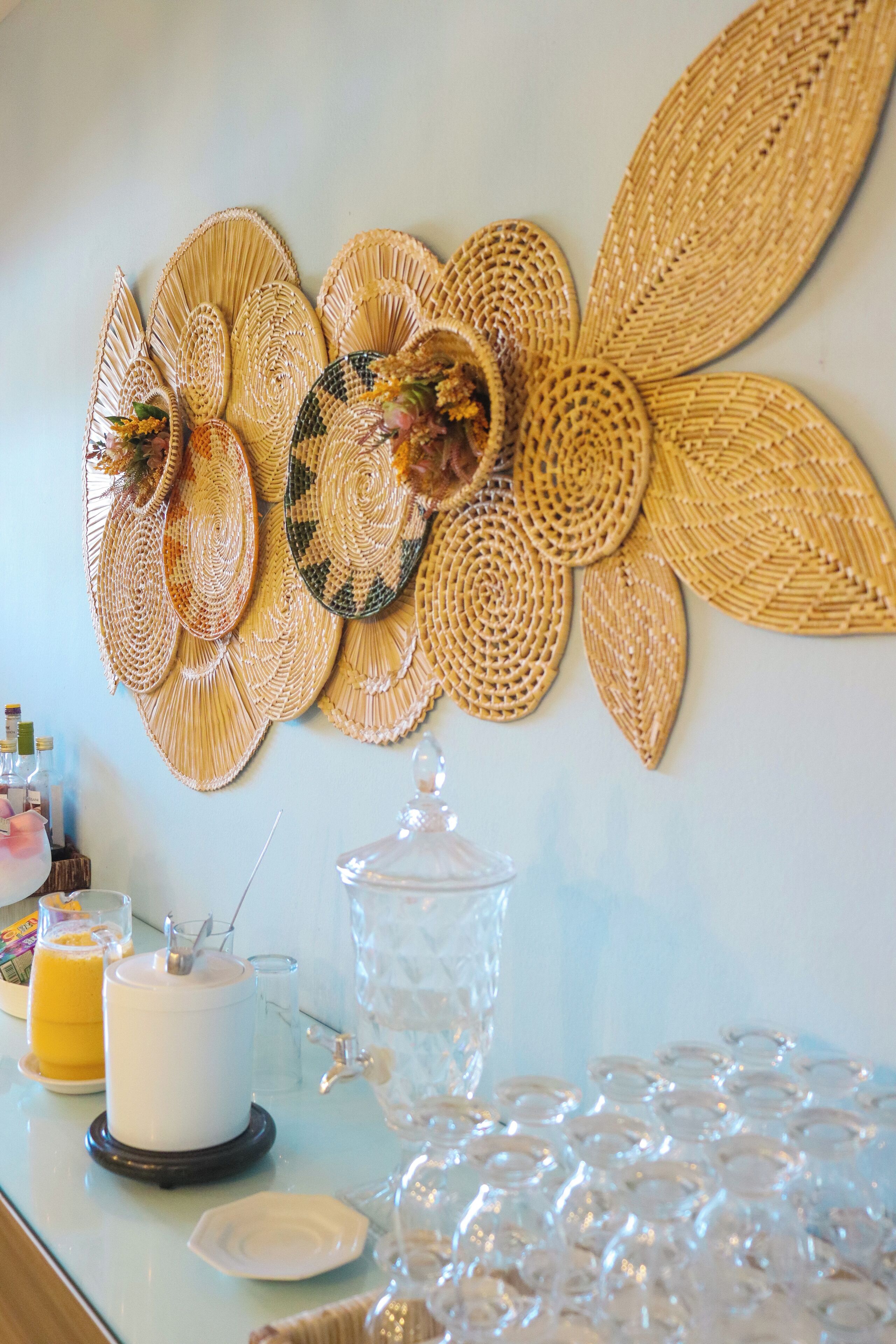Pared decorada con patrones circulares tejidos, un recipiente de vidrio y una mesa con una jarra de vidrio transparente y una botella.