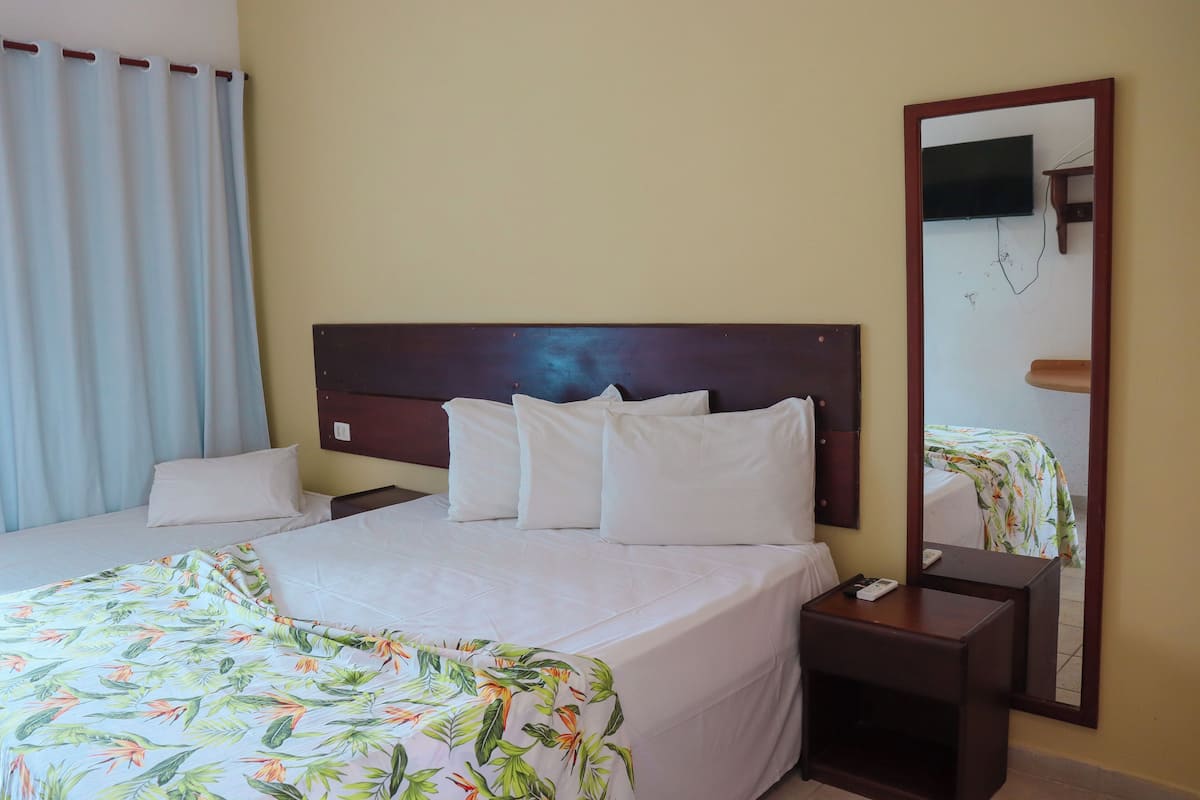 Een hotelkamer met een groot bed, een nachtkastje, een spiegel en een aan de muur bevestigde televisie.