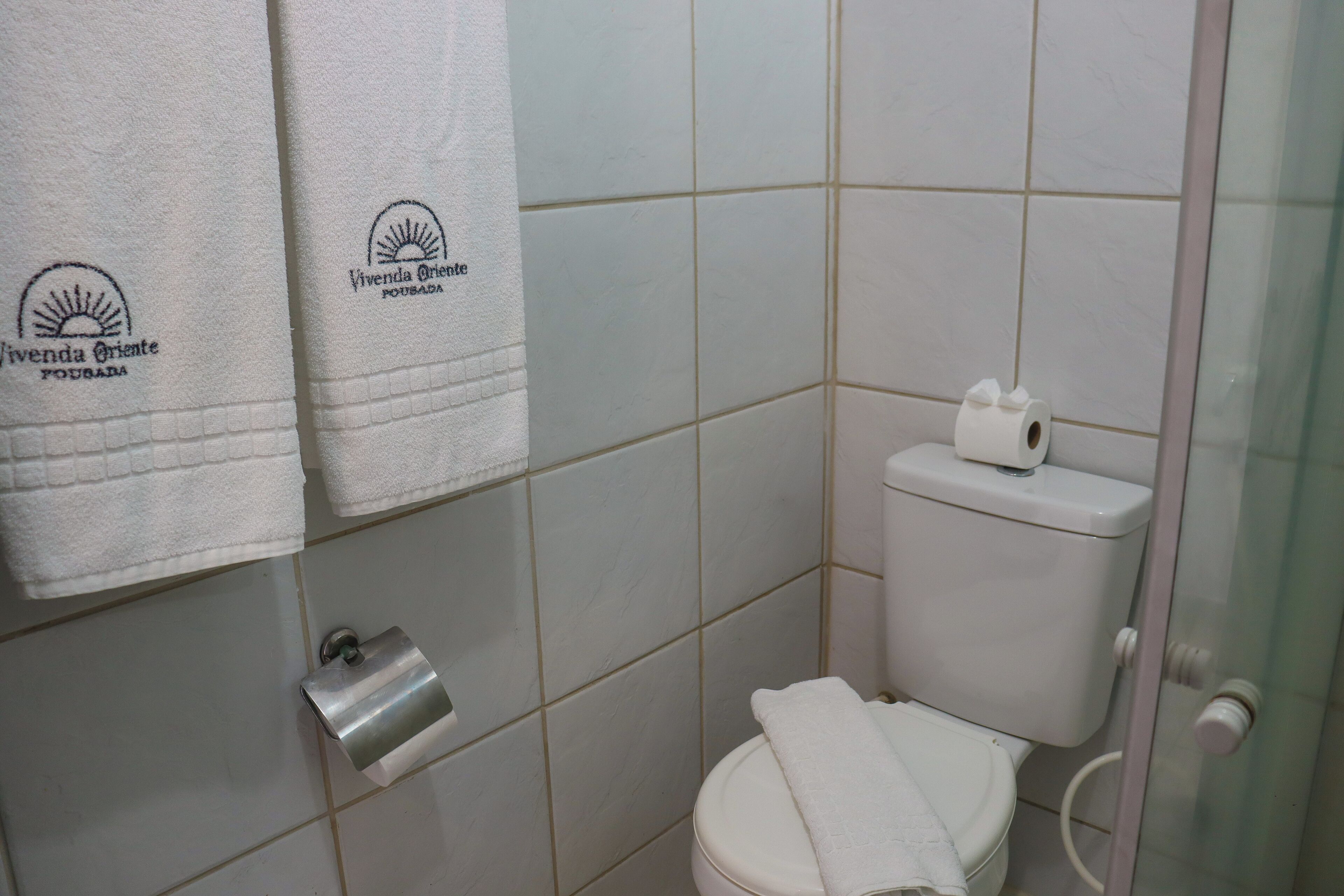 A bathroom with a toilet, a paper towel dispenser, and two towels hanging on the wall.