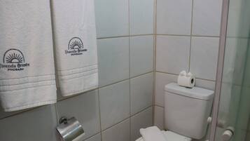 A bathroom with a toilet, a paper towel dispenser, and two towels hanging on the wall.
