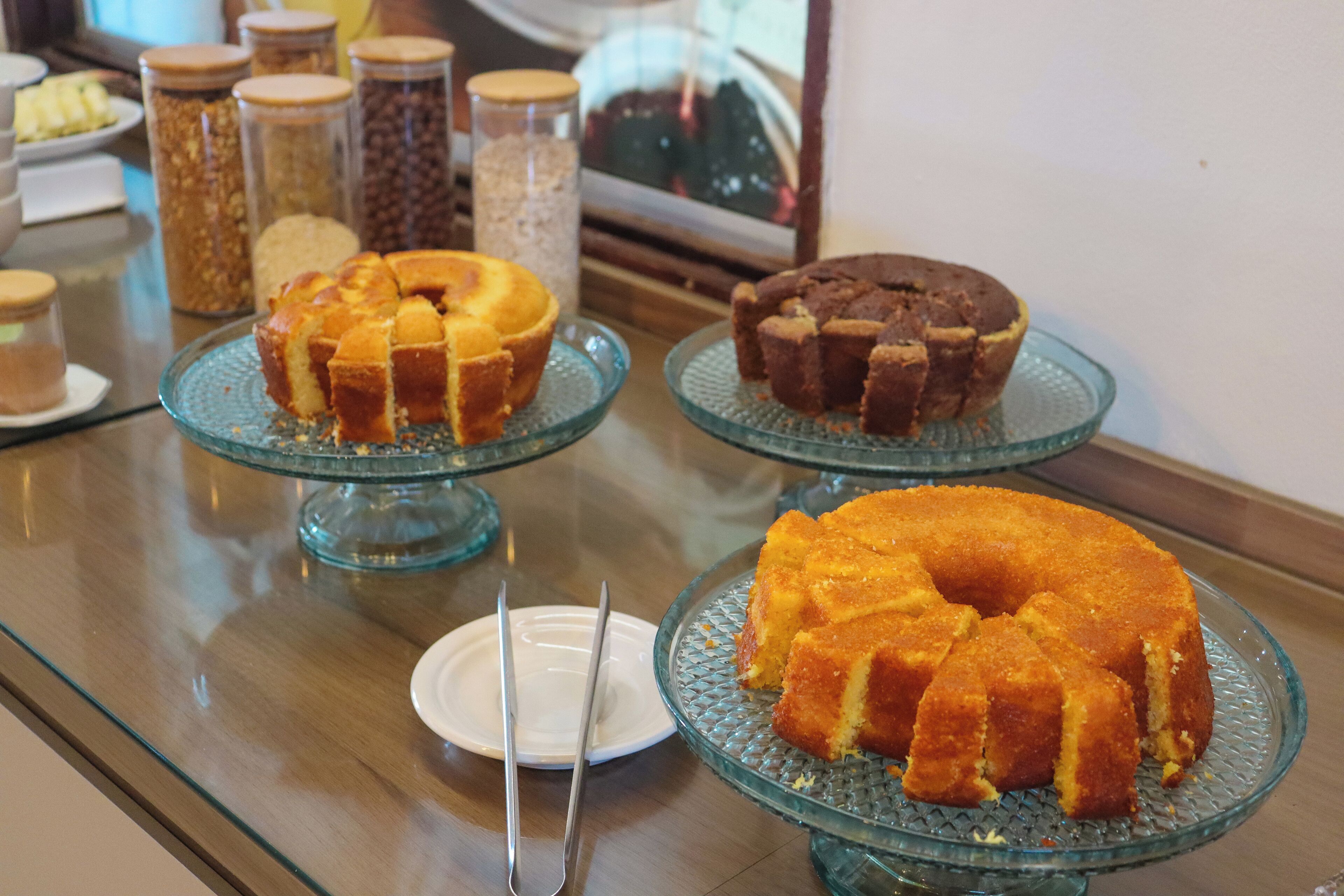 A buffet table with various baked goods on glass stands, including a bundt cake, muffins, and a slice of cake on a plate.
