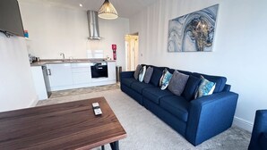 A modern living room with a blue sofa, a wooden coffee table, and a kitchen in the background.