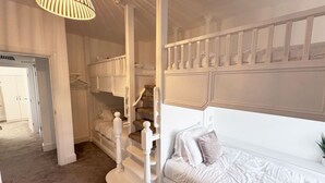 A bedroom with a bed, a window with a plant, a staircase, and a door leading to another room.