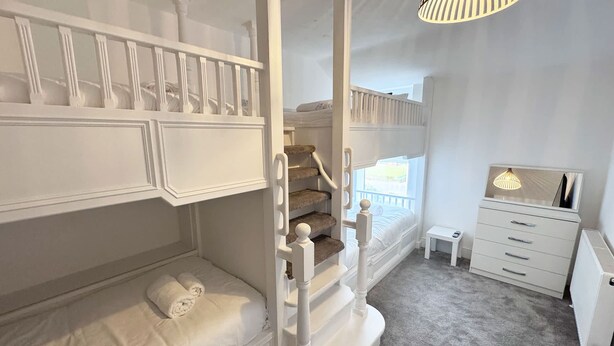 A bedroom with a bunk bed, a small bedside table, a dresser, and a staircase.