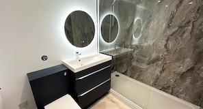 Une salle de bain moderne avec un mur en marbre, un miroir rond, un lavabo blanc et un meuble-lavabo noir.