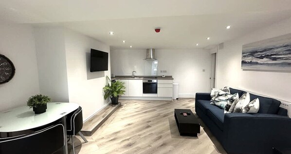 Un salon moderne comprenant un canapé, une table à manger avec des chaises, un coin cuisine avec une cuisinière et un évier, et un téléviseur à écran plat fixé au mur.