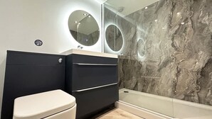 A modern bathroom with a toilet, dark vanity, and a glass shower enclosure.