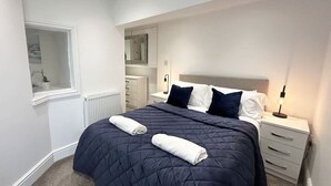 A bedroom with a bed, two bedside tables, a window, a mirror, and a radiator.