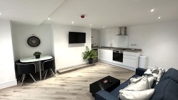 A modern kitchen with a built-in oven and microwave, a dining area with a round table and chairs, and a living room with a sofa and coffee table.