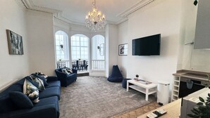 Una sala moderna con un sofá azul oscuro, una mesa de centro blanca y un televisor montado en la pared.