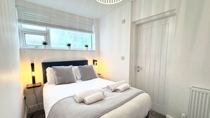 Un dormitorio con cama, lámparas de noche, una ventana con persianas y una puerta.