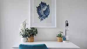 A white desk with a framed artwork, two potted plants, a teal chair, and a floor lamp. - Heritage on Liebig - Perch at the top of town (Warrnambool)