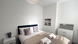 Ein ordentlich eingerichtetes Schlafzimmer mit Bett, Nachttischen, einem Fernseher und einem Bild an der Wand.