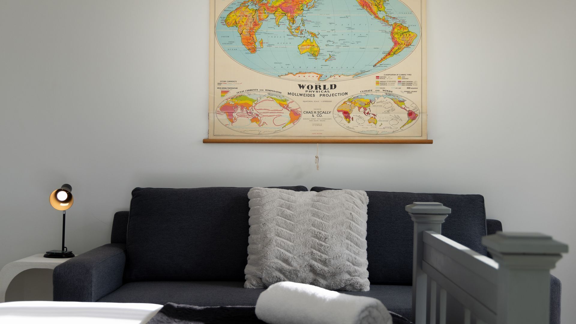 Une pièce avec un canapé bleu foncé, un coussin blanc, une carte du monde accrochée au mur et un lampadaire.