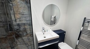 Ein Badezimmer mit Marmorwand, Waschbecken inklusive Spiegel und Handtuchhalter.