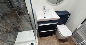 Ein Badezimmer mit einer Marmordusche, einem weiĂen Waschbecken mit Toilettenartikeln, einem schwarzen Schrank und einer weiĂen Toilette.