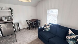 A compact living space with a kitchenette, a dining area, and a seating area with a sofa and chairs. - The Little Tern - A Cosy Coastal Retreat (Lancashire)