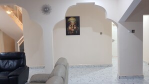 A hallway with a marble floor, a black leather chair, and a painting on the wall. - Serenity Villa in Sunny Burusbi Phase 2 (Sukuta)