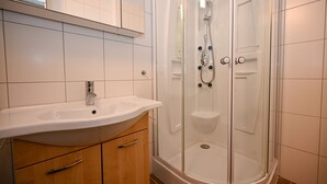 A modern bathroom with a glass-enclosed shower, a white sink, and wooden cabinets. - Domizil Alpine Retreat 15 With Balcony (Kaprun)