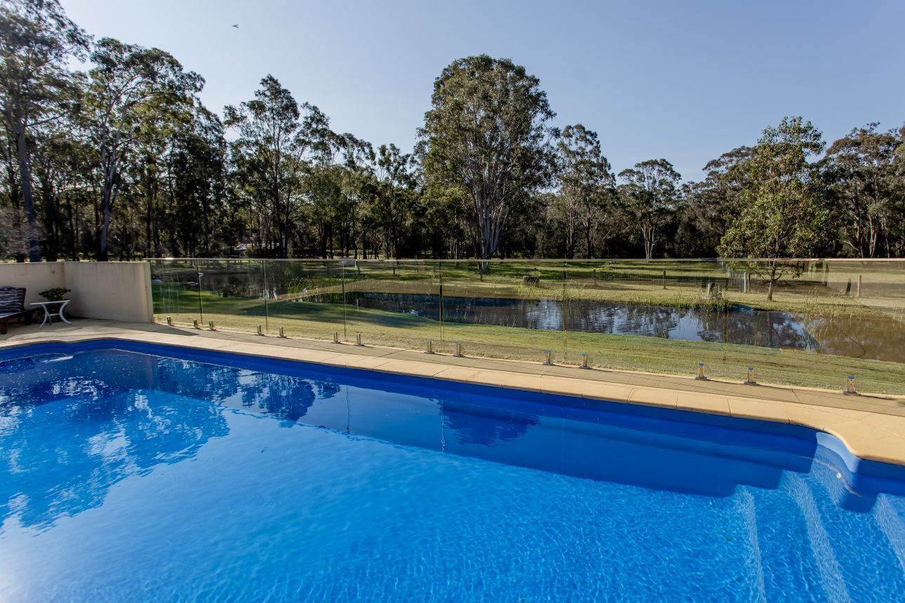 A swimming pool with a clear view of the surrounding landscape, including trees and a grassy area.