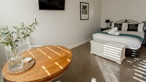 Ein Schlafzimmer mit einem Bett, Nachttischen, einem Fernseher, einem gerahmten Foto und einem runden Holztisch mit einer Pflanze.