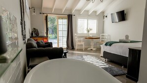 A modern hotel room with a large bathtub, a bed, a dining area, and a view of the outdoors.