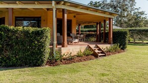 A covered outdoor seating area with chairs and a table, surrounded by a well-maintained lawn and hedges.