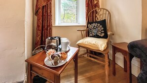 A cozy room with a wooden chair, a small table with a plate of pastries, a cup, and a kettle. - 3 bedroom accommodation in Colwyn Bay (Colwyn Bay)