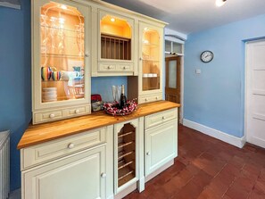 Une cuisine avec un plan de travail en bois, un meuble vitré contenant des ustensiles de cuisine et une horloge au mur.
