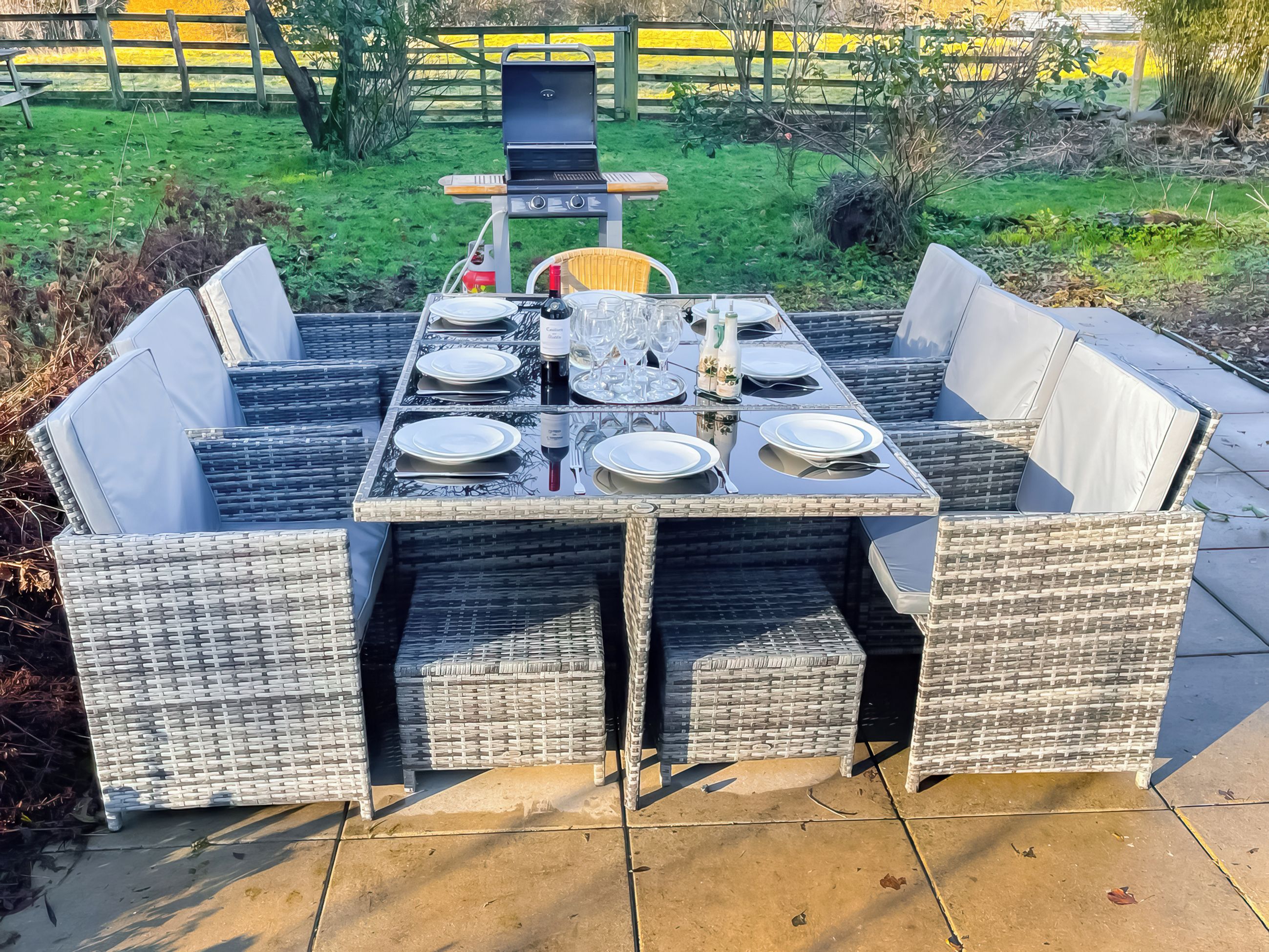 A rectangular outdoor dining table with four chairs, surrounded by a garden.