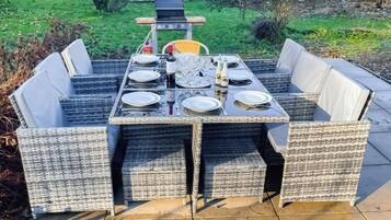 A rectangular outdoor dining table with four chairs, surrounded by a garden.