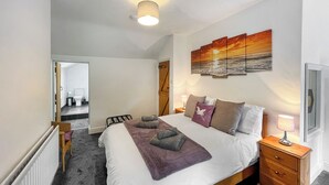 A bedroom with a bed, bedside table, lamp, and a painting on the wall. - 3 bedroom accommodation in Colwyn Bay (Colwyn Bay)