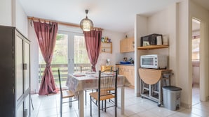 A kitchen with a dining table, chairs, a microwave, and a trash bin.