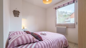A bedroom with a bed, pillows, a bedside lamp, a window, and a wall decoration.