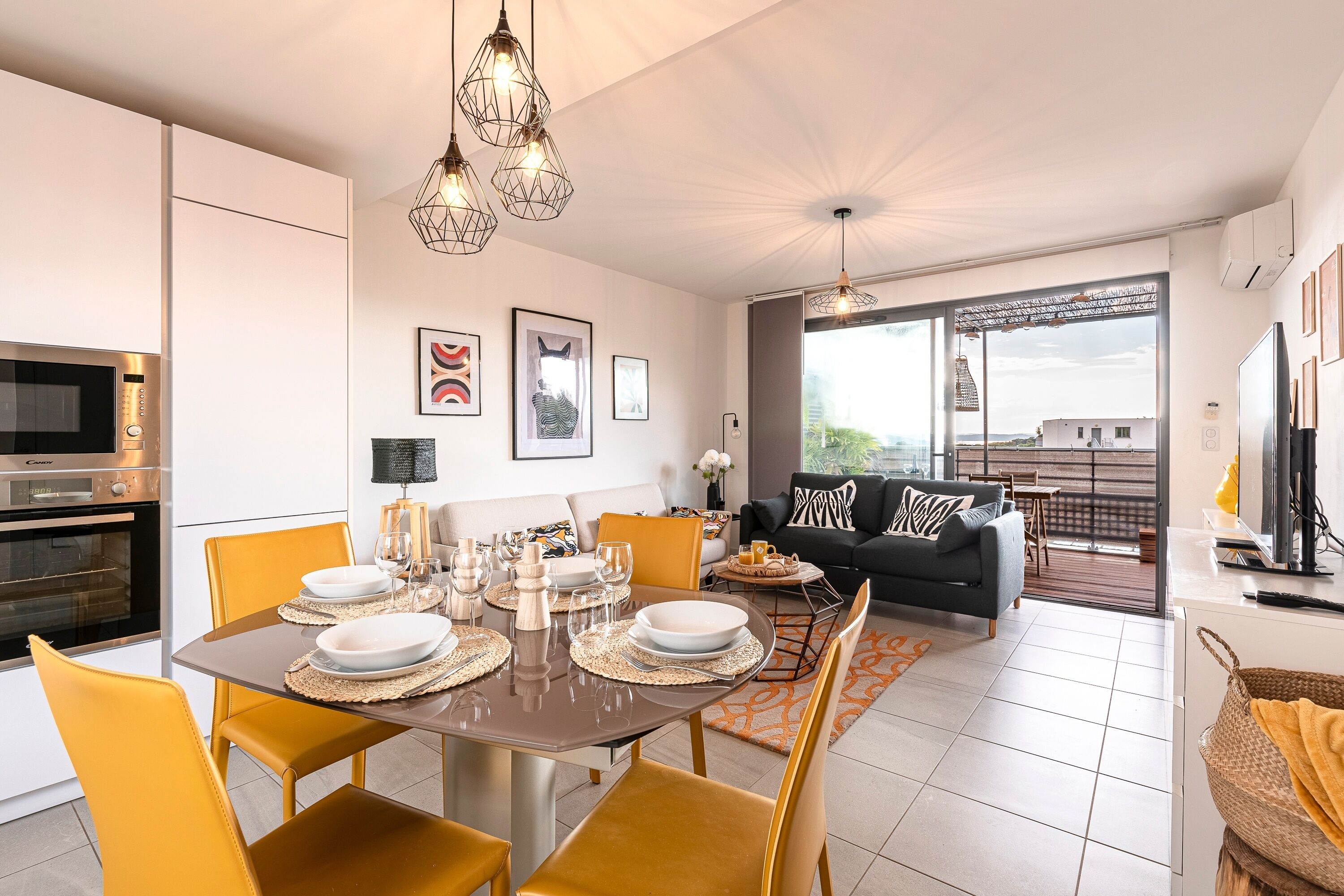 Une cuisine moderne dotée d’un four encastré et d’un coin repas avec des chaises jaunes et une table dressée pour quatre personnes.